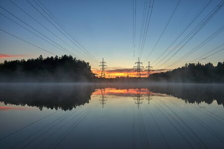 High voltage power lines reflected in a foggy lake at sunset
