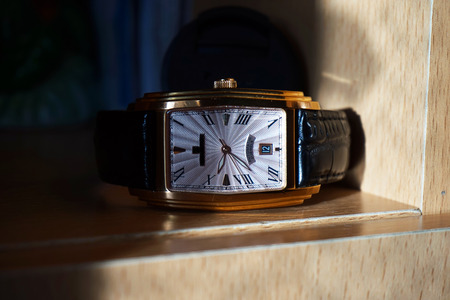  Wristwatch with leather strap on a wooden shelf. Style of the barrel clock, gold-plated case, dial,...