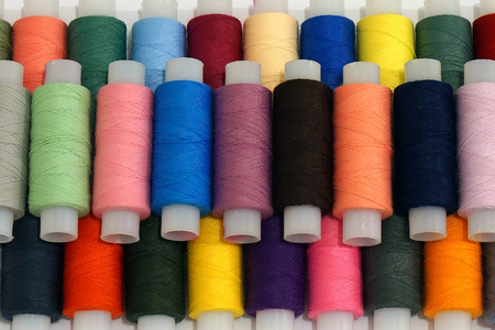 Background with a lot of colorful coils with threads. Bobbins are stacked in three rows, one on the...