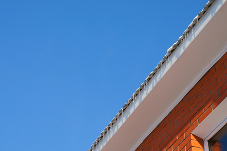 sunny day, blue sky. On the roof of the house the snow melts, flows and turns into icicles. House of...