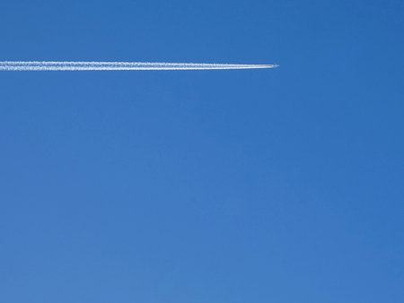 The plane flies high in the blue sky and leaves a white trail.                               
