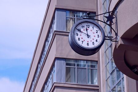 Street round clock on the background of high urban buildings. Arrows, numbers, home warm colors.の写真素材