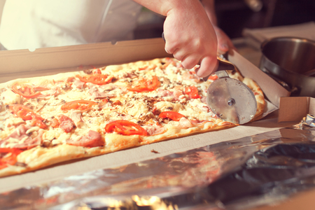 Closeup hand of chef baker in white uniform cutting pizza at kitchen.の写真素材