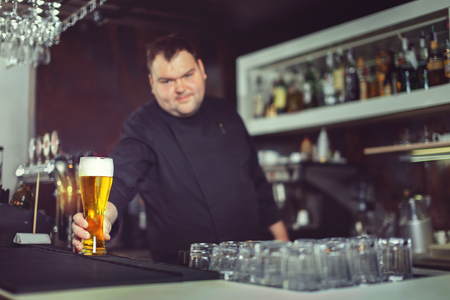 Close-up of young bartender pouring beer while standing at the bar counter.の写真素材
