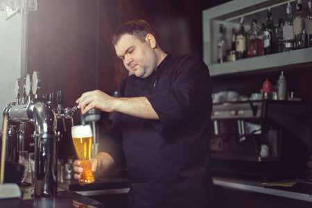 Close-up of young bartender pouring beer while standing at the bar counter.の写真素材