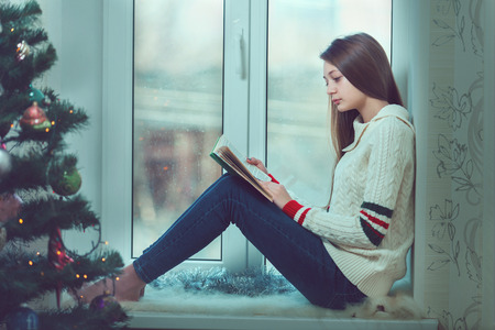 Young beautiful woman with reddish hair sitting home by the windowの写真素材