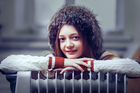 Girl in mittens and hats bask near radiatoの写真素材
