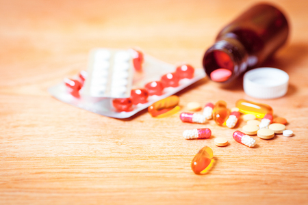 Medication spilling from an open bottle on a wooden background.の写真素材