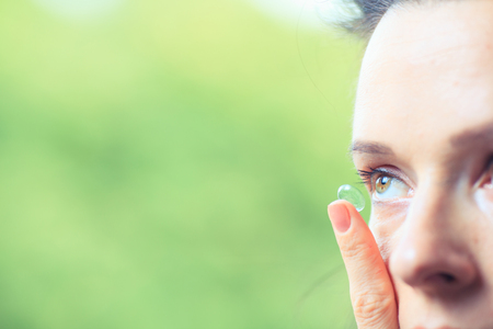 Young brunette woman holding contact lens on finger in front of her eyeの写真素材