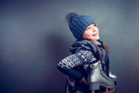 Cheerful little girl in warm sweater and hat holding figure skates.