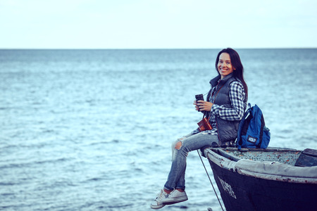 happy stylish woman hipster holding photo camera and smiling at sunny shore near water, summer...