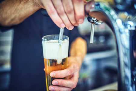 Close-up of young bartender pouring beer while standing at the bar counter.の写真素材