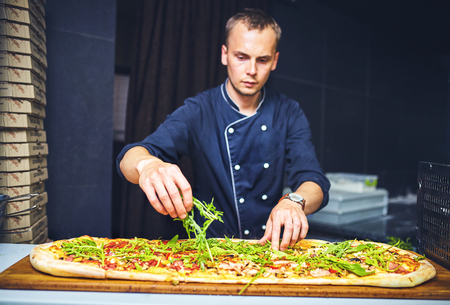 chef baker cook in black uniform putting pizza into the oven with shovel at restaurant kitchen.の写真素材