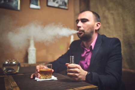 vaping man holding a mechanical mod. A cloud of vapor.の写真素材