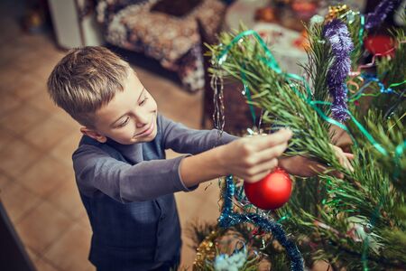 Happy child decorates a Christmas tree in the houseの写真素材