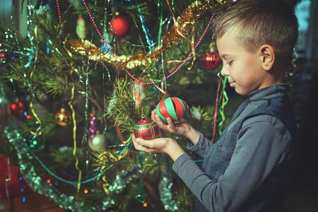 Happy child decorates a Christmas tree in the houseの写真素材