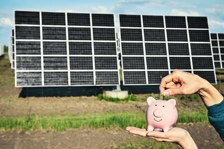 Hand holding money banknote with photovoltaic solar energy panels in background,の写真素材