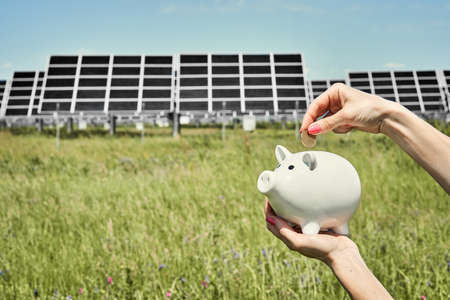 Hand holding money banknote with photovoltaic solar energy panels in background,の写真素材