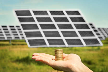 Hand holding money banknote with photovoltaic solar energy panels in background,