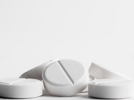 White round tablets on a white background. A pile of small round medicines close up. Healthcare and...