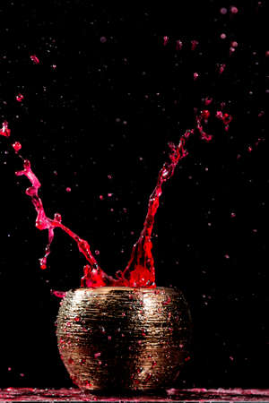 Water mixed with lighter fluid inside a golden pot throwing ice stone to cause thermal shock and cause a splash of liquid with fire on the black background.の写真素材