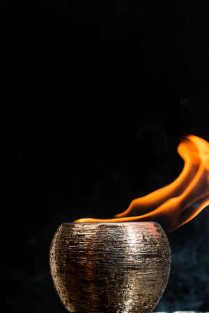 Water mixed with lighter fluid inside a golden pot throwing ice stone to cause thermal shock and cause a splash of liquid with fire on the black background.の写真素材
