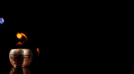 Water mixed with lighter fluid inside a golden pot throwing ice stone to cause thermal shock and cause a splash of liquid with fire on the black background.の写真素材