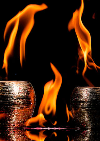 Water mixed with lighter fluid inside a golden pot throwing ice stone to cause thermal shock and cause a splash of liquid with fire on the black background.の写真素材