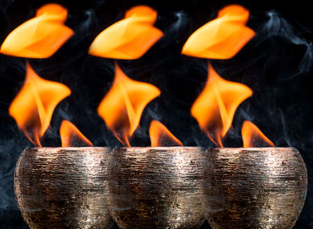 Water mixed with lighter fluid inside a golden pot throwing ice stone to cause thermal shock and cause a splash of liquid with fire on the black background.の写真素材