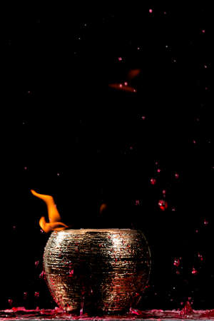 Water mixed with lighter fluid inside a golden pot throwing ice stone to cause thermal shock and cause a splash of liquid with fire on the black background.の写真素材