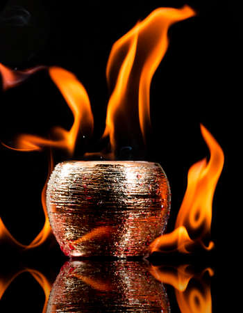 Water mixed with lighter fluid inside a golden pot throwing ice stone to cause thermal shock and cause a splash of liquid with fire on the black background.の写真素材
