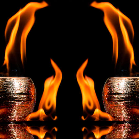 Water mixed with lighter fluid inside a golden pot throwing ice stone to cause thermal shock and cause a splash of liquid with fire on the black background.の写真素材