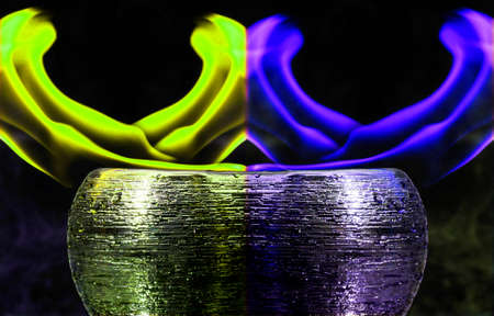 Water mixed with lighter fluid inside a golden pot throwing ice stone to cause thermal shock and cause a splash of liquid with fire on the black background.の写真素材