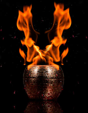 Water mixed with lighter fluid inside a golden pot throwing ice stone to cause thermal shock and cause a splash of liquid with fire on the black background.の写真素材