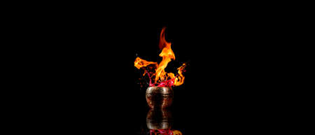 Water mixed with lighter fluid inside a golden pot throwing ice stone to cause thermal shock and cause a splash of liquid with fire on the black background.の写真素材