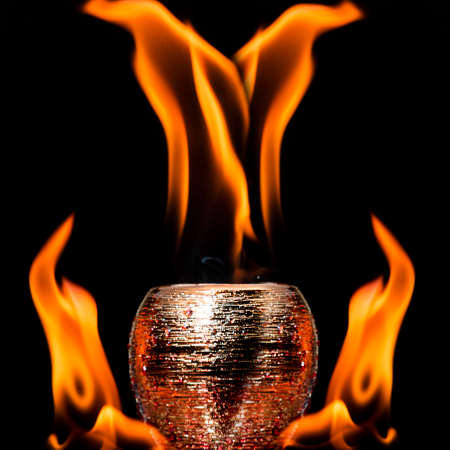 Water mixed with lighter fluid inside a golden pot throwing ice stone to cause thermal shock and cause a splash of liquid with fire on the black background.の写真素材