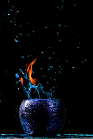Water mixed with lighter fluid inside a golden pot throwing ice stone to cause thermal shock and cause a splash of liquid with fire on the black background.の写真素材