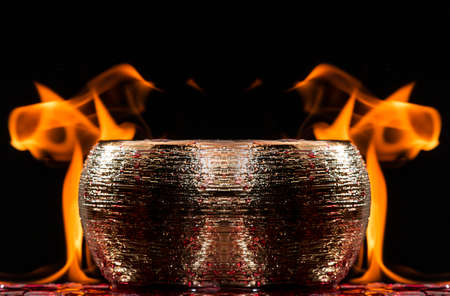 Water mixed with lighter fluid inside a golden pot throwing ice stone to cause thermal shock and cause a splash of liquid with fire on the black background.の写真素材