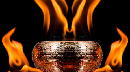 Water mixed with lighter fluid inside a golden pot throwing ice stone to cause thermal shock and cause a splash of liquid with fire on the black background.の写真素材