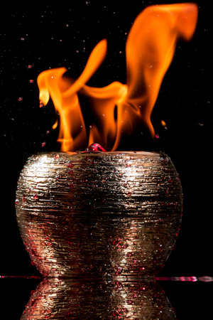 Water mixed with lighter fluid inside a golden pot throwing ice stone to cause thermal shock and cause a splash of liquid with fire on the black background.の写真素材