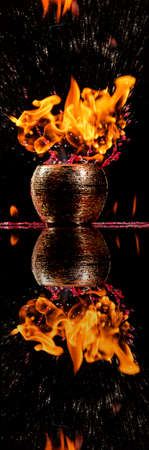 Water mixed with lighter fluid inside a golden pot throwing ice stone to cause thermal shock and cause a splash of liquid with fire on the black background.の写真素材