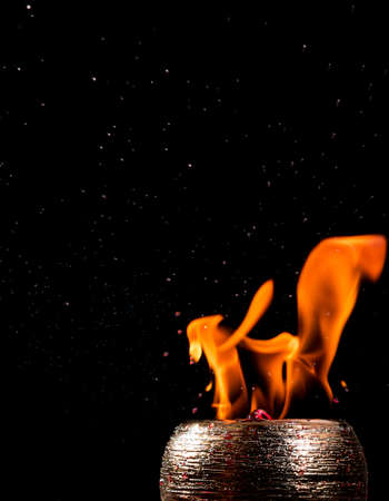 Water mixed with lighter fluid inside a golden pot throwing ice stone to cause thermal shock and cause a splash of liquid with fire on the black background.の写真素材