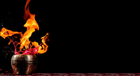 Water mixed with lighter fluid inside a golden pot throwing ice stone to cause thermal shock and cause a splash of liquid with fire on the black background.の写真素材