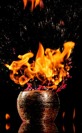 Water mixed with lighter fluid inside a golden pot throwing ice stone to cause thermal shock and cause a splash of liquid with fire on the black background.の写真素材