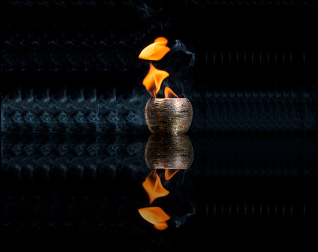 Water mixed with lighter fluid inside a golden pot throwing ice stone to cause thermal shock and cause a splash of liquid with fire on the black background.の写真素材
