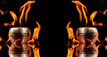 Water mixed with lighter fluid inside a golden pot throwing ice stone to cause thermal shock and cause a splash of liquid with fire on the black background.の写真素材