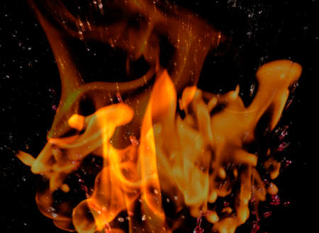 Water mixed with lighter fluid inside a golden pot throwing ice stone to cause thermal shock and cause a splash of liquid with fire on the black background.の写真素材
