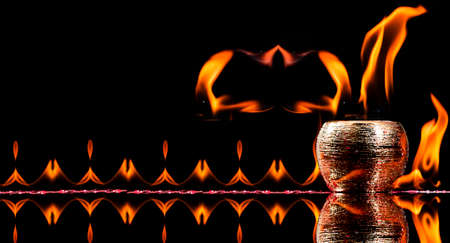 Water mixed with lighter fluid inside a golden pot throwing ice stone to cause thermal shock and cause a splash of liquid with fire on the black background.の写真素材