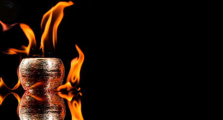 Water mixed with lighter fluid inside a golden pot throwing ice stone to cause thermal shock and cause a splash of liquid with fire on the black background.の写真素材