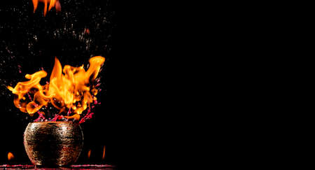 Water mixed with lighter fluid inside a golden pot throwing ice stone to cause thermal shock and cause a splash of liquid with fire on the black background.の写真素材